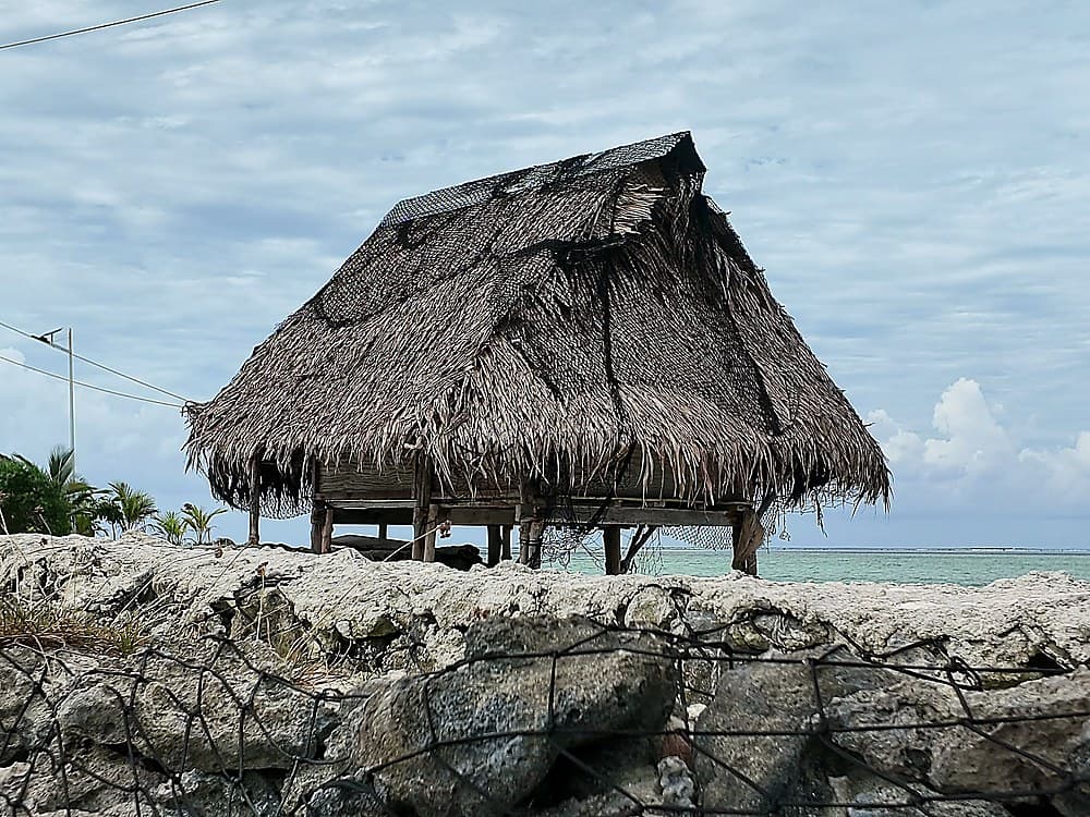 A palm-thatch hut and the lagoon beyond a stone wall